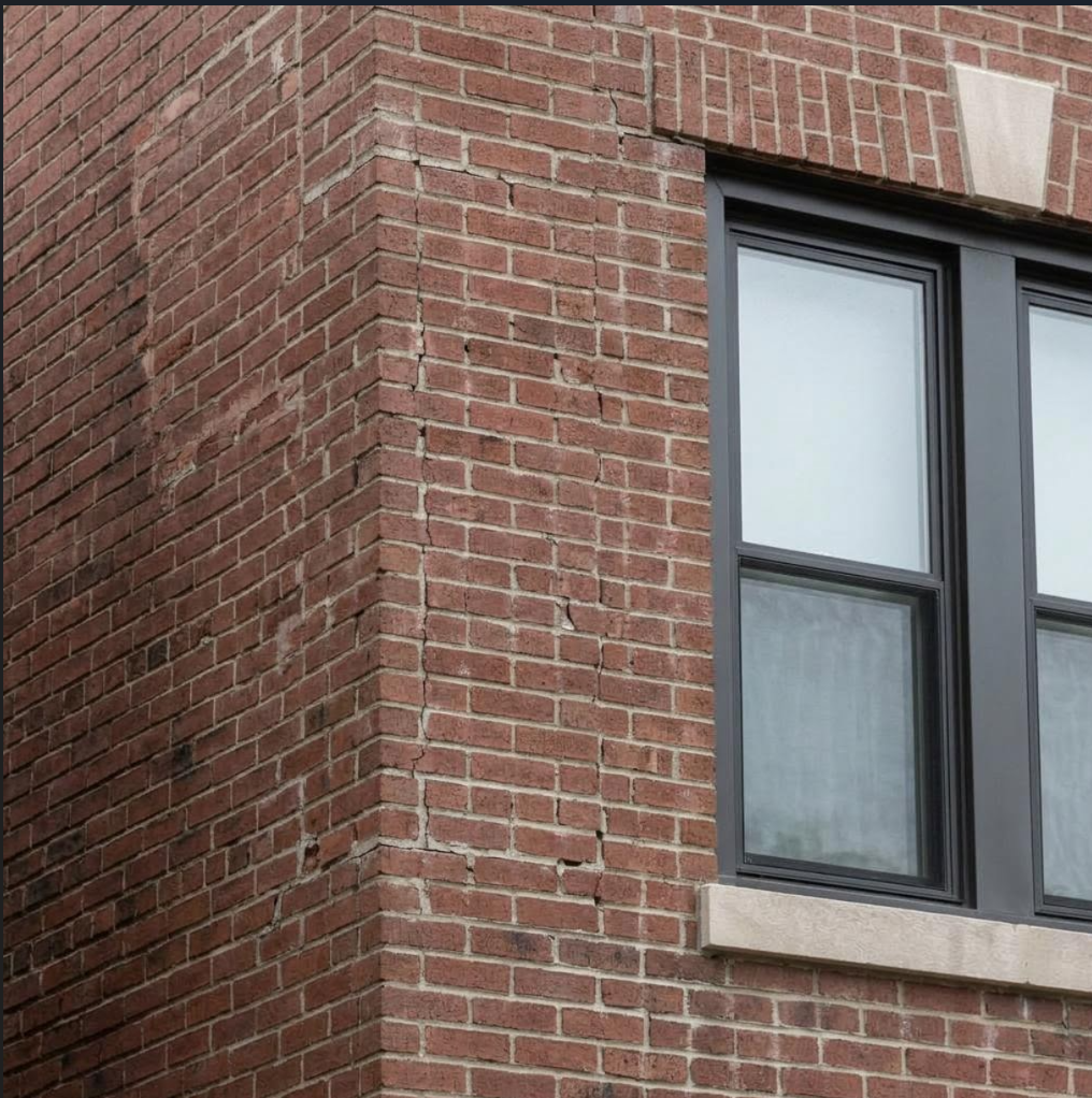 Damaged brick and mortar beside a window before facade repairs in Middle Village